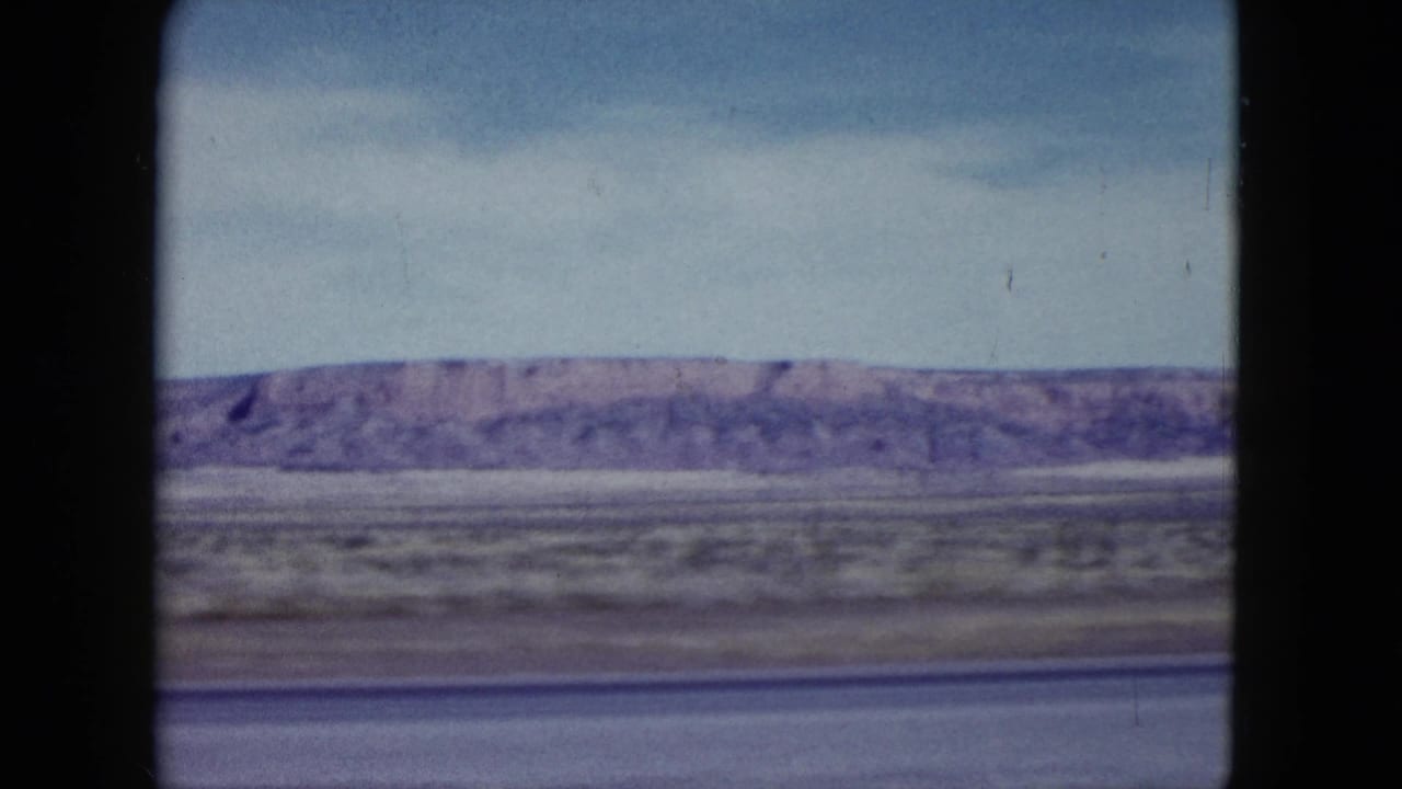 Final 1959 Nevada roadside frame with a low desert ridge, muted scrubland, pale sky, and dark film-window borders.