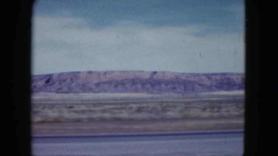Final 1959 Nevada roadside frame with a low desert ridge, muted scrubland, pale sky, and dark film-window borders.