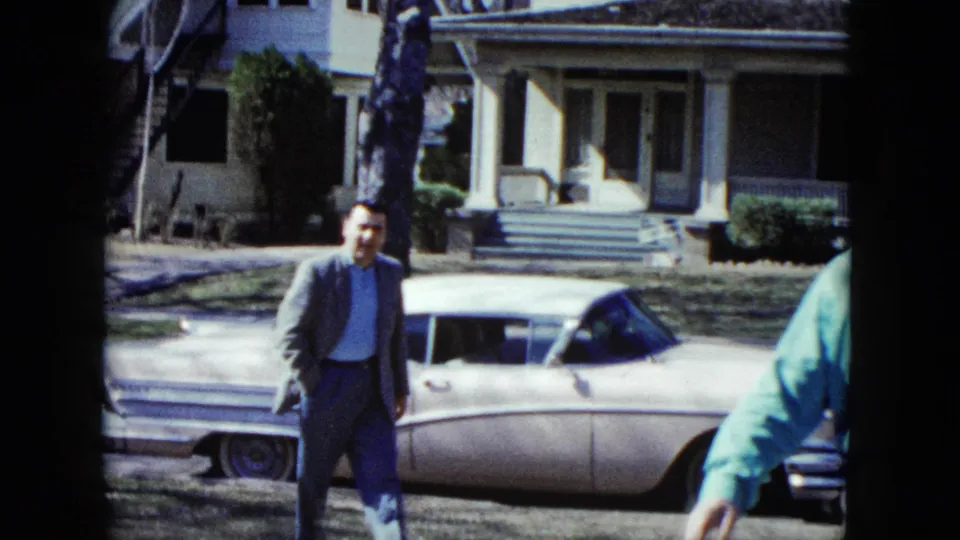 In the final Nevada 1959 frame, the suited man is close to the foreground beside the white sedan with its hood open, while a man in a green shirt is partly visible at the right edge of the suburban scene.