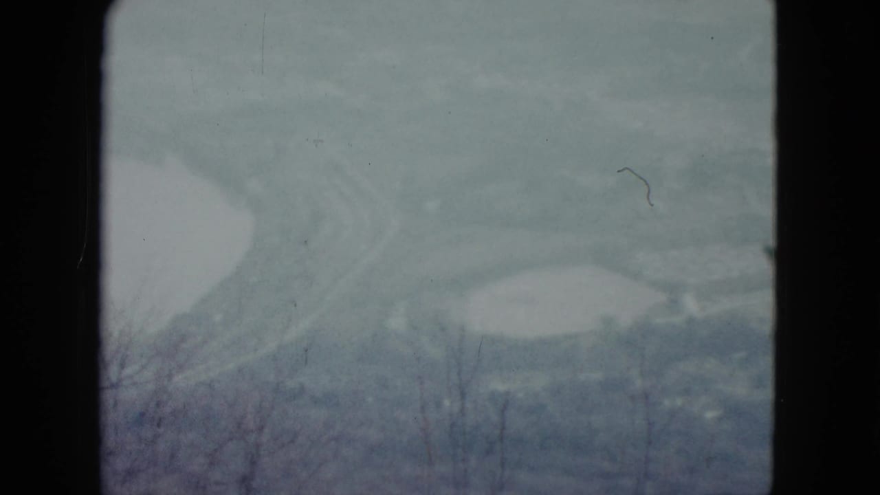 Hazy valley seen from a hillside with pale water basins, bare branches, and dark film borders.