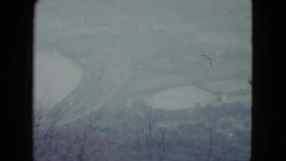 1959 Nevada 8mm frame showing a misty valley overlook with pale reservoir-like shapes, foreground branches, and dark gate edges.
