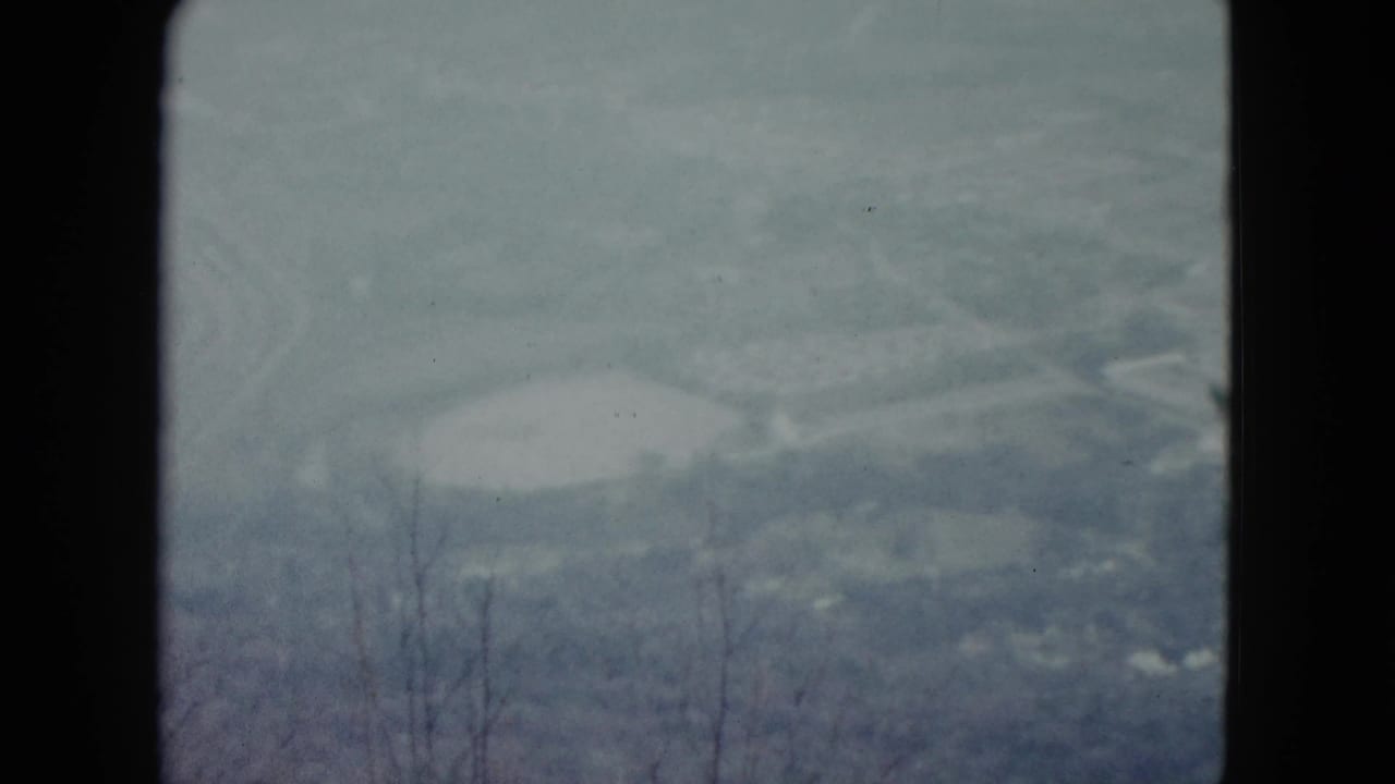 Soft distant landscape with pale basin shapes, winding terrain lines, and dark film-frame edges.