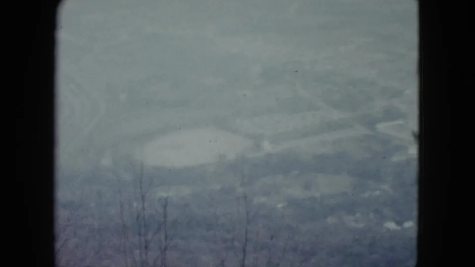 1959 Nevada home-movie frame with a soft valley view, pale reservoir-like areas, distant roads or ridges, and visible 8mm frame borders.