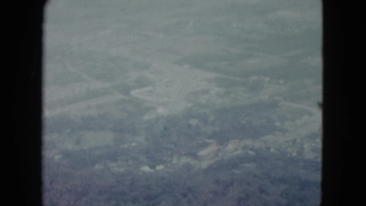 1959 Nevada 8mm frame showing a hazy aerial view of farmland and scattered trees through a window frame.