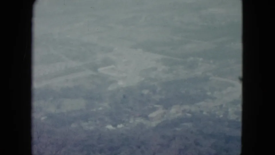 1959 Nevada 8mm frame showing a hazy aerial view of farmland and scattered trees through a window frame.