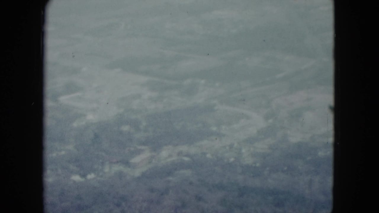 A soft 1959 Nevada aerial frame with fields, faint roads, and cloud haze visible through the window.