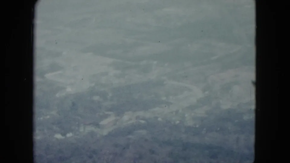 A soft 1959 Nevada aerial frame with fields, faint roads, and cloud haze visible through the window.