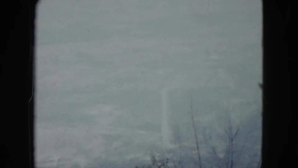 1959 Nevada 8mm view of a muted, haze-filled horizon with faint terrain and sparse bare branches near the frame edge.