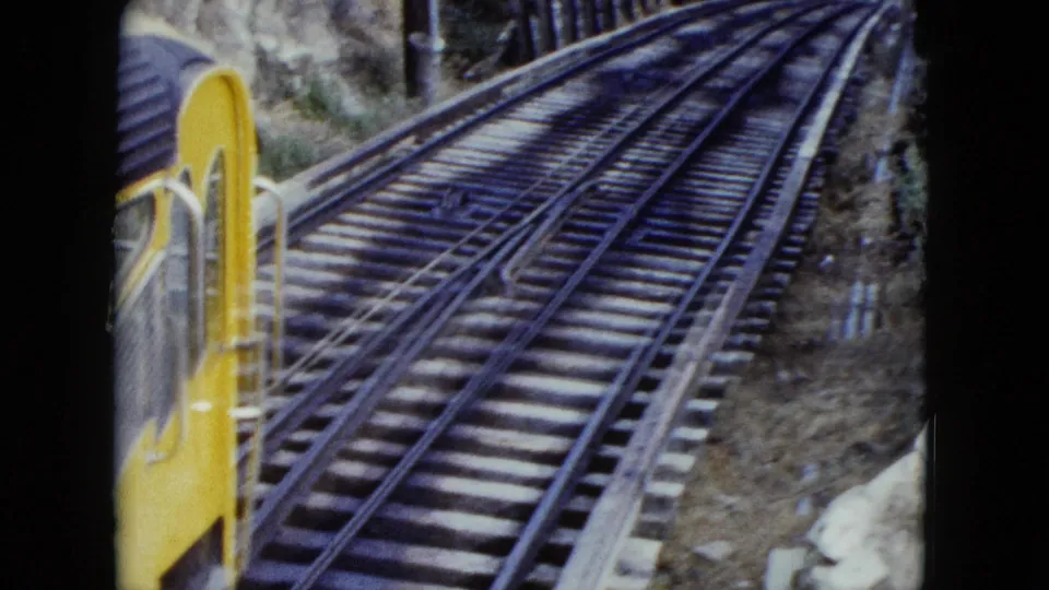 1959 Nevada 8mm frame looking past the yellow incline car toward steep rails climbing through a wooded hillside.