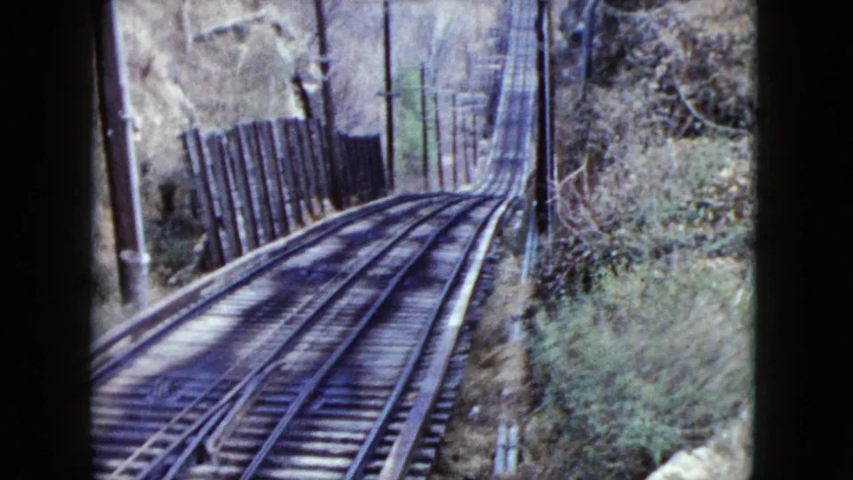 1959 Nevada 8mm frame showing incline railway tracks curving upward through brush with fencing or a gate near the right side.