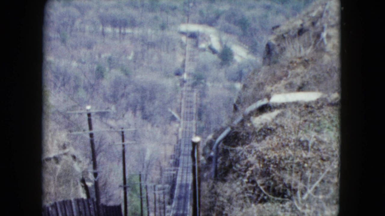1959 Nevada rail view with descending track corridor, utility poles, rocky brush, and muted wooded hills beyond.