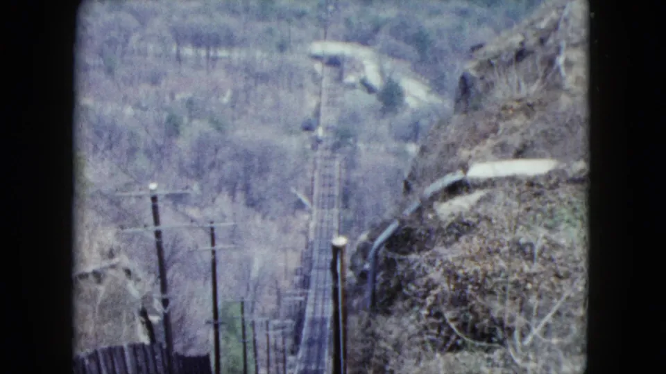 1959 Nevada rail view with descending track corridor, utility poles, rocky brush, and muted wooded hills beyond.