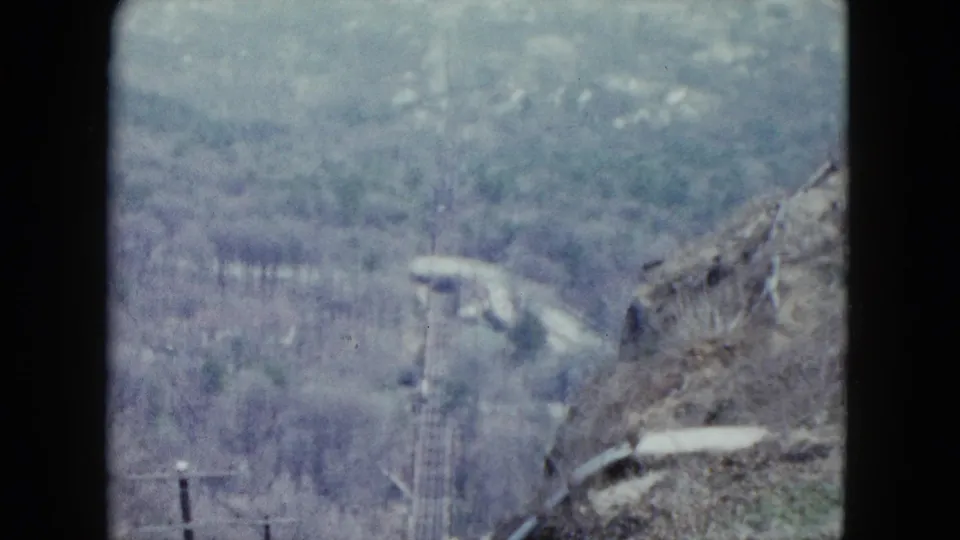 Soft 1959 Nevada 8mm frame showing utility poles, wooded terrain, and brush along a descending rail route.
