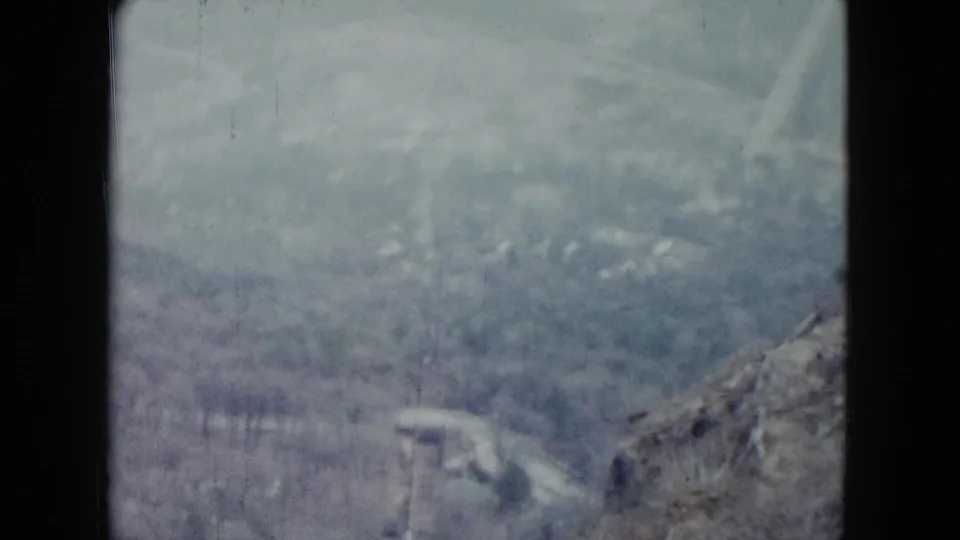 Faded 1959 Nevada 8mm view of a brushy hillside and utility poles near the descending railway.