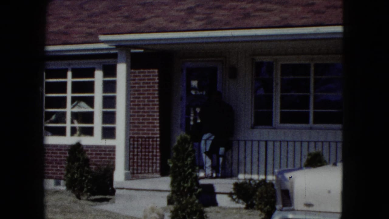 Older man standing in the doorway of a suburban brick-and-siding house.