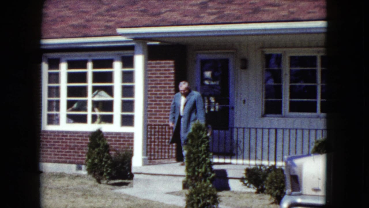 Older man stepping from the porch beside a white-trimmed window and shrubs.