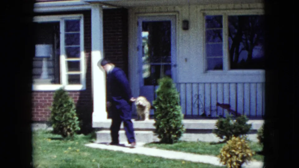 The suited man steps away from the porch of a Nevada suburban home in 1959 while a small dog stays by the open doorway.