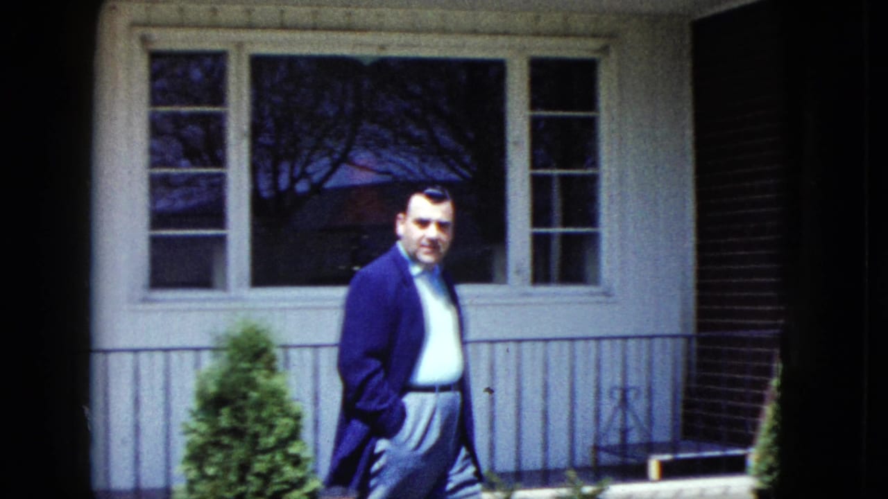 Man in a dark coat walking near the front windows of a house.