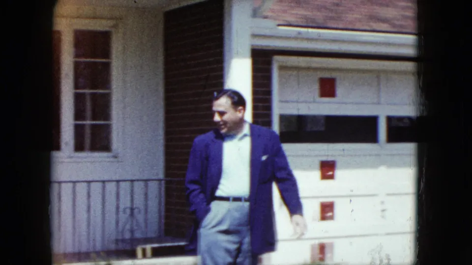 An adult man in dress clothes walks near a white garage door and brick wall in the Nevada residential scene.