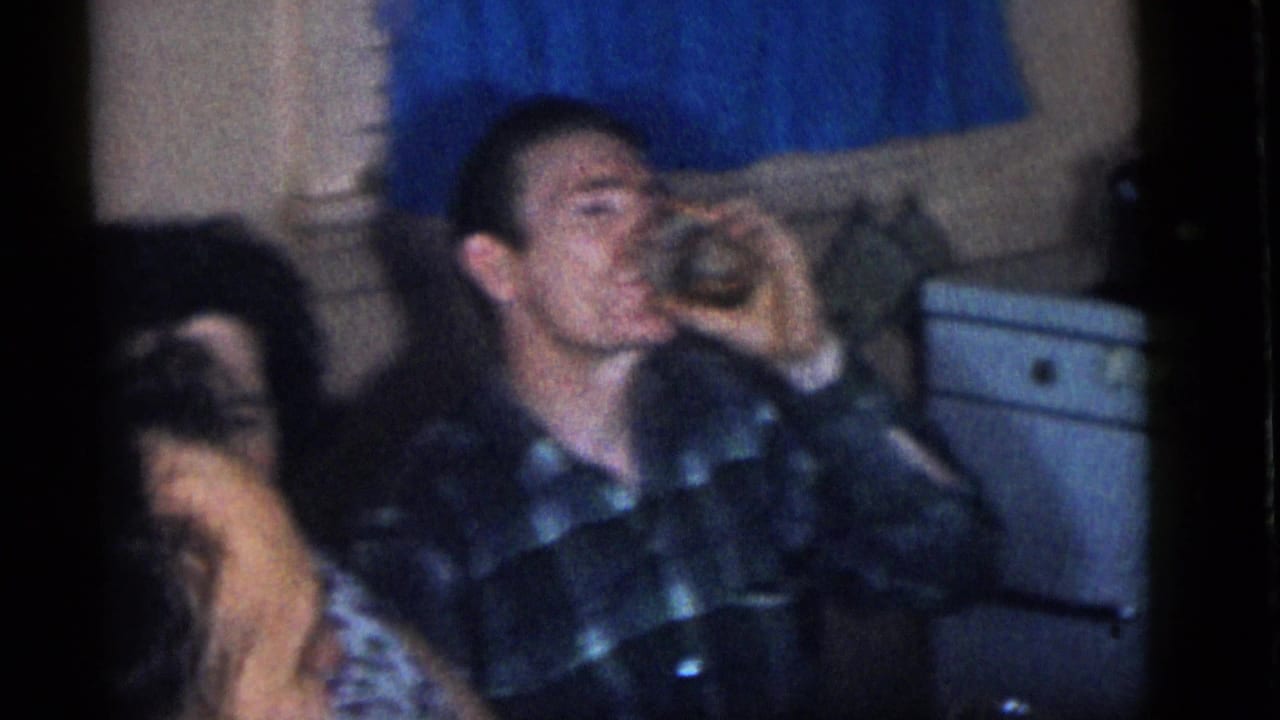 Inside a Camden, New Jersey home in 1960, a man in a plaid shirt drinks at a casual lunch table as another adult sits in the foreground.