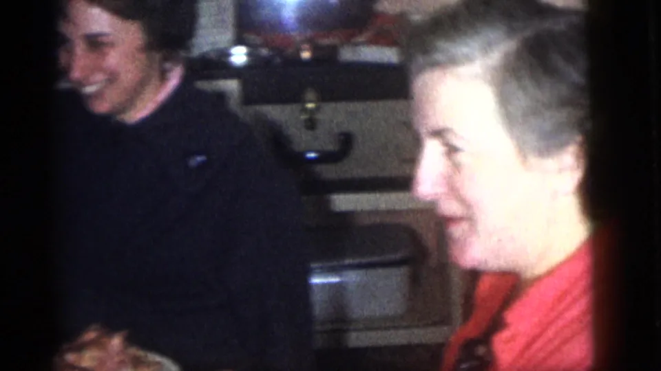 Two adults appear to laugh or talk at the lunch table inside the Camden home, including a woman in a red top seen in profile.