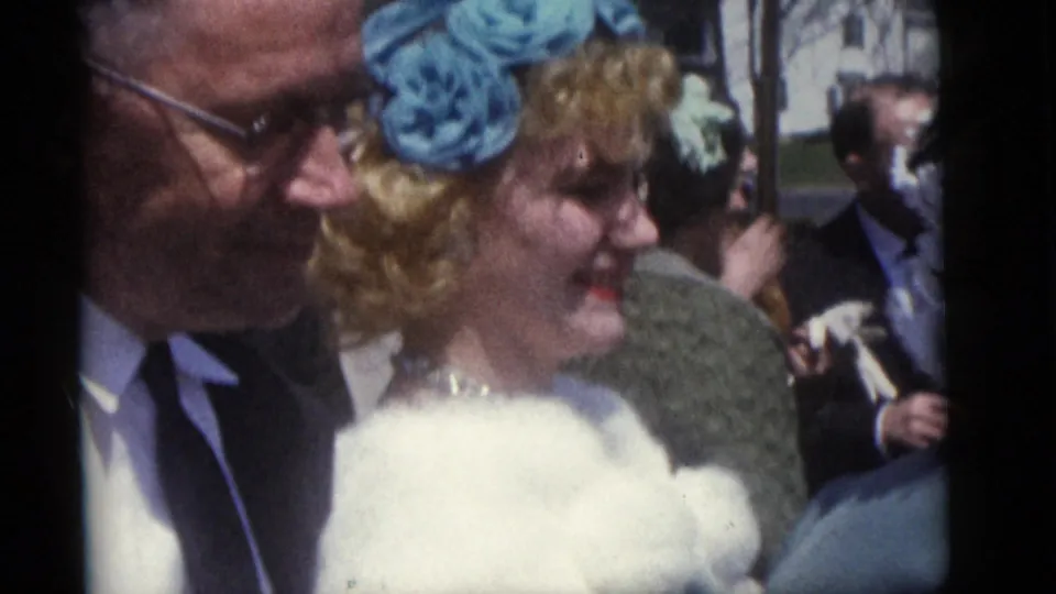 Guests in formal dress, including a woman with a blue hat and fur stole, smile during the 1960 Camden wedding gathering.
