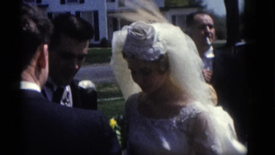 The bride and groom face a suited man in the Camden, New Jersey wedding footage, with guests and buildings visible behind them.