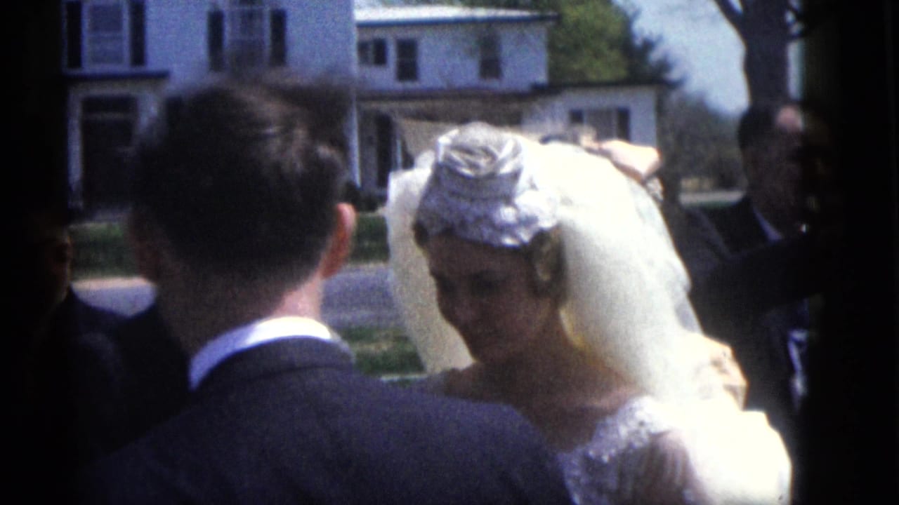 Bride faces the groom during an outdoor ceremony with guests and houses behind them.