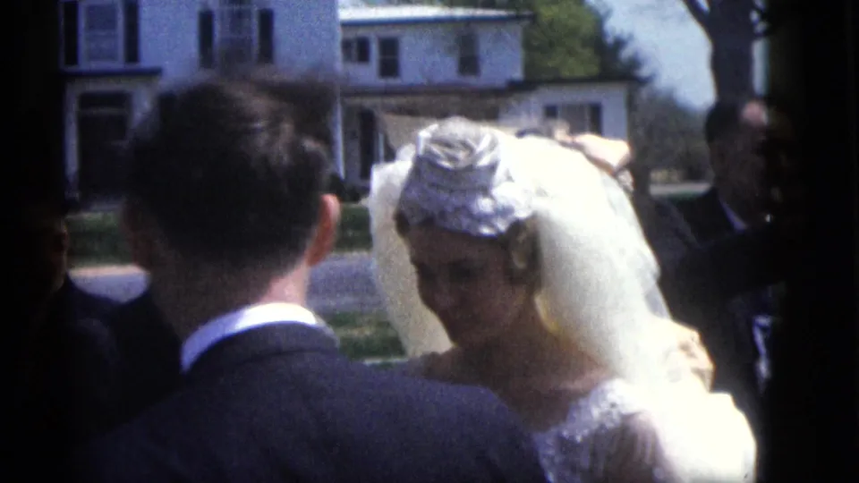 The bride and groom appear in profile during a Camden outdoor wedding ceremony, with guests and suburban houses in the background.