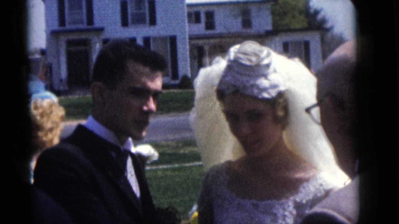 The groom in a dark suit and the bride in a lace gown stand together in 1960 Camden wedding home-movie footage.