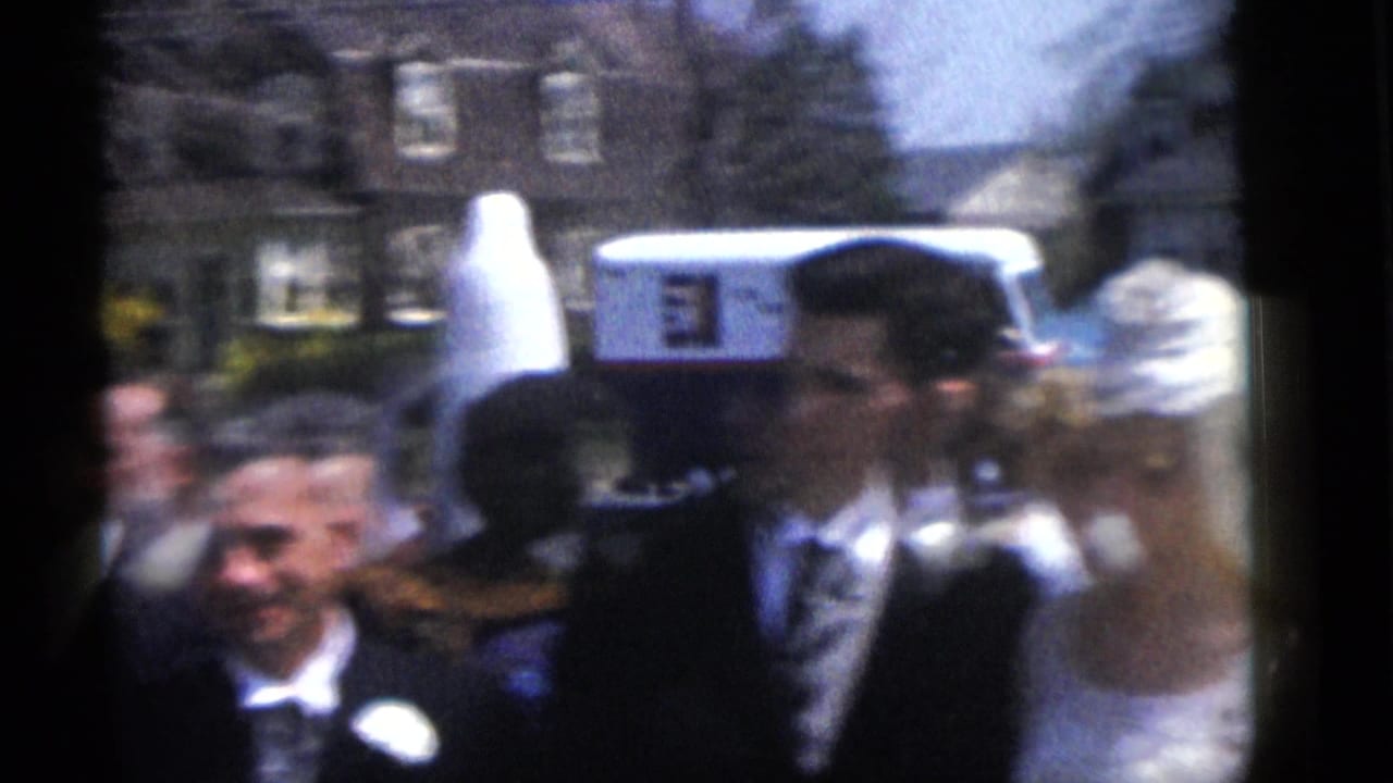 1960 Camden, New Jersey home-movie frame showing a wedding party passing outside houses in bright daylight.