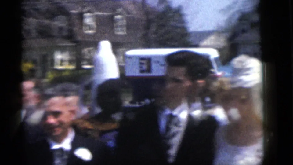 1960 Camden, New Jersey home-movie frame showing a wedding party passing outside houses in bright daylight.