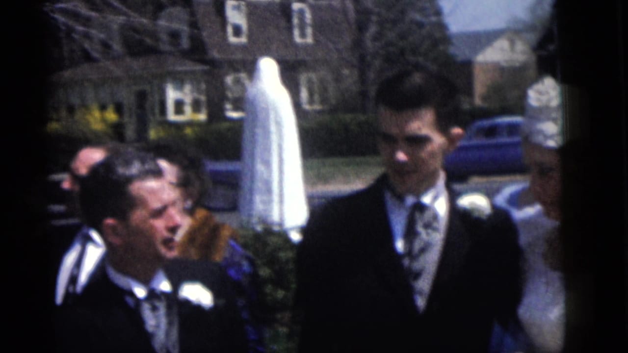 End frame of the 1960 Camden wedding procession with groom, guests, and bride partly visible outdoors.