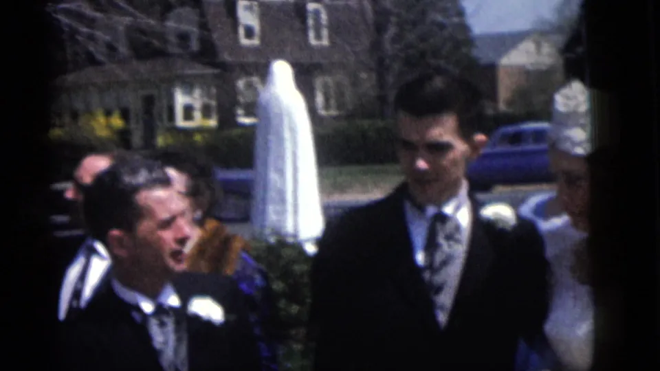 End frame of the 1960 Camden wedding procession with groom, guests, and bride partly visible outdoors.