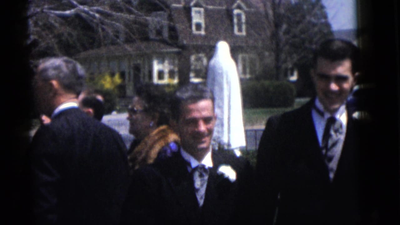 Groomsmen and guests stand outside near a bride in a veil and a white statue.