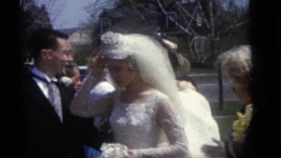 The bride adjusts her long veil beside the groom during a 1960 outdoor wedding moment in Camden, New Jersey.