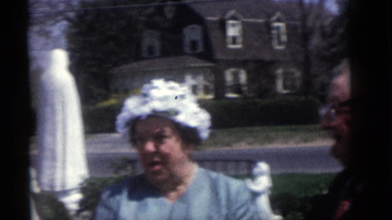 In the 1960 Camden wedding footage, a woman in a white hat stands outdoors with a suited man partly visible beside her.