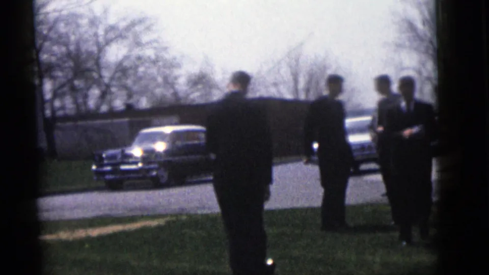 Men in formal suits stand outside during the Camden wedding gathering, with mid-century cars parked near the road.