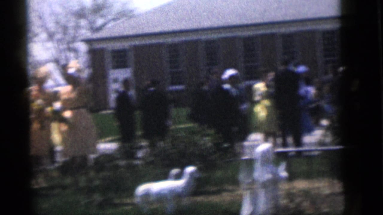 Guests at the 1960 Camden wedding gather near the brick building, with white lamb figurines visible on the lawn in front.