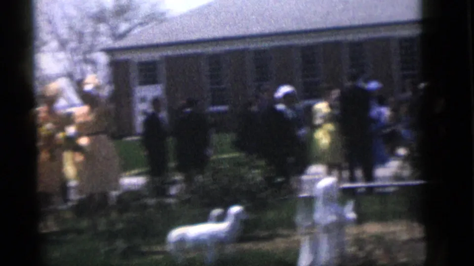 Guests at the 1960 Camden wedding gather near the brick building, with white lamb figurines visible on the lawn in front.