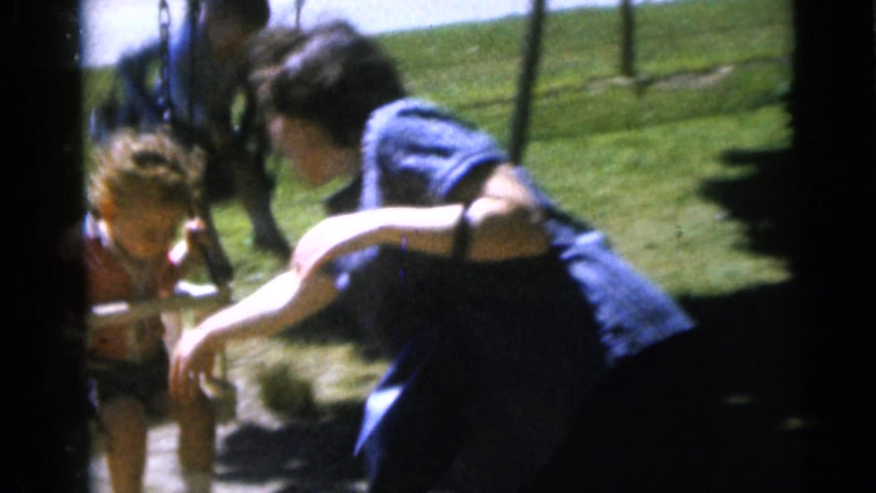 Two people outdoors near a swing and grassy area in soft 8mm footage.