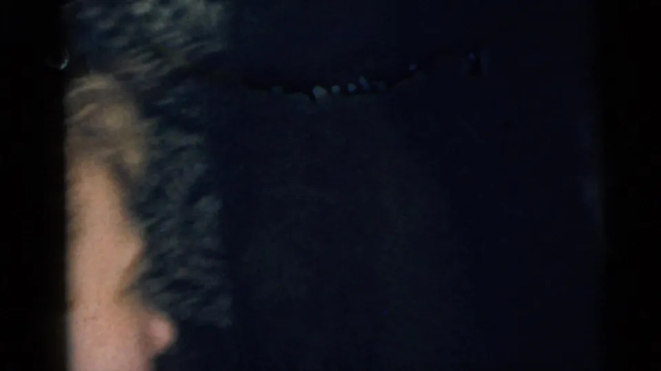 A dark final home-movie frame from the Camden clip shows a partial face and indistinct patterned texture in very low indoor light.