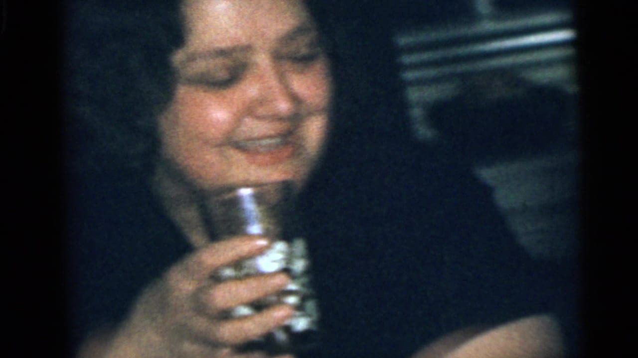 Adult woman laughs while holding a glass close to her chest.
