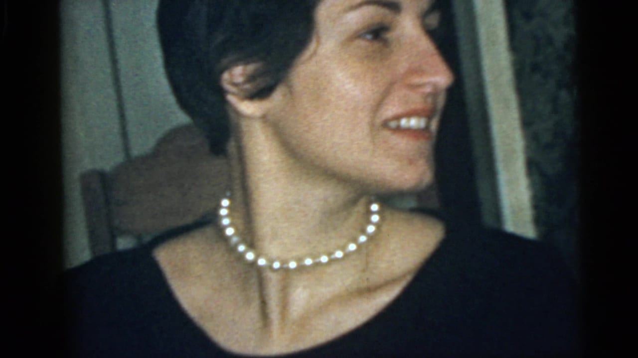 Adult woman in a dark top and pearl necklace smiles in close-up, consistent with the 1960 Camden home-movie metadata.