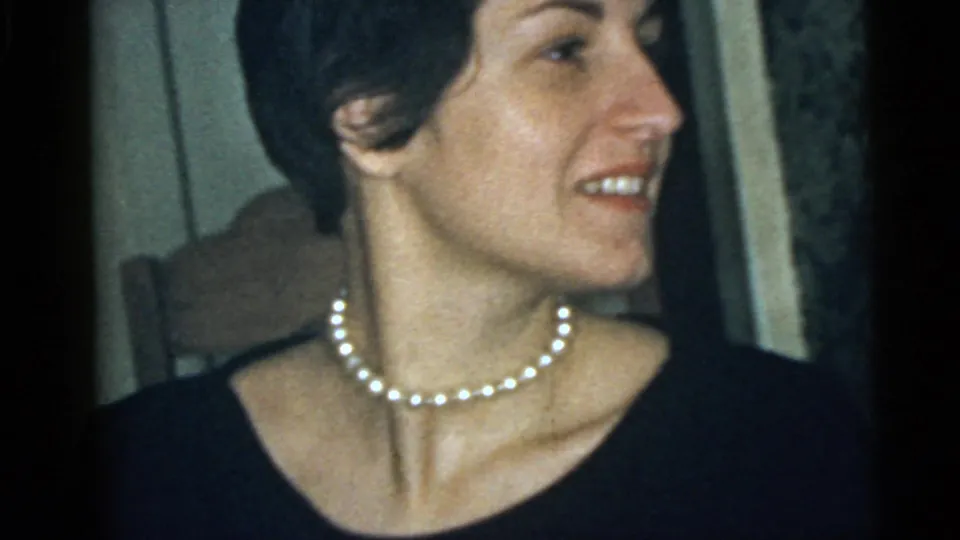Adult woman in a dark top and pearl necklace smiles in close-up, consistent with the 1960 Camden home-movie metadata.
