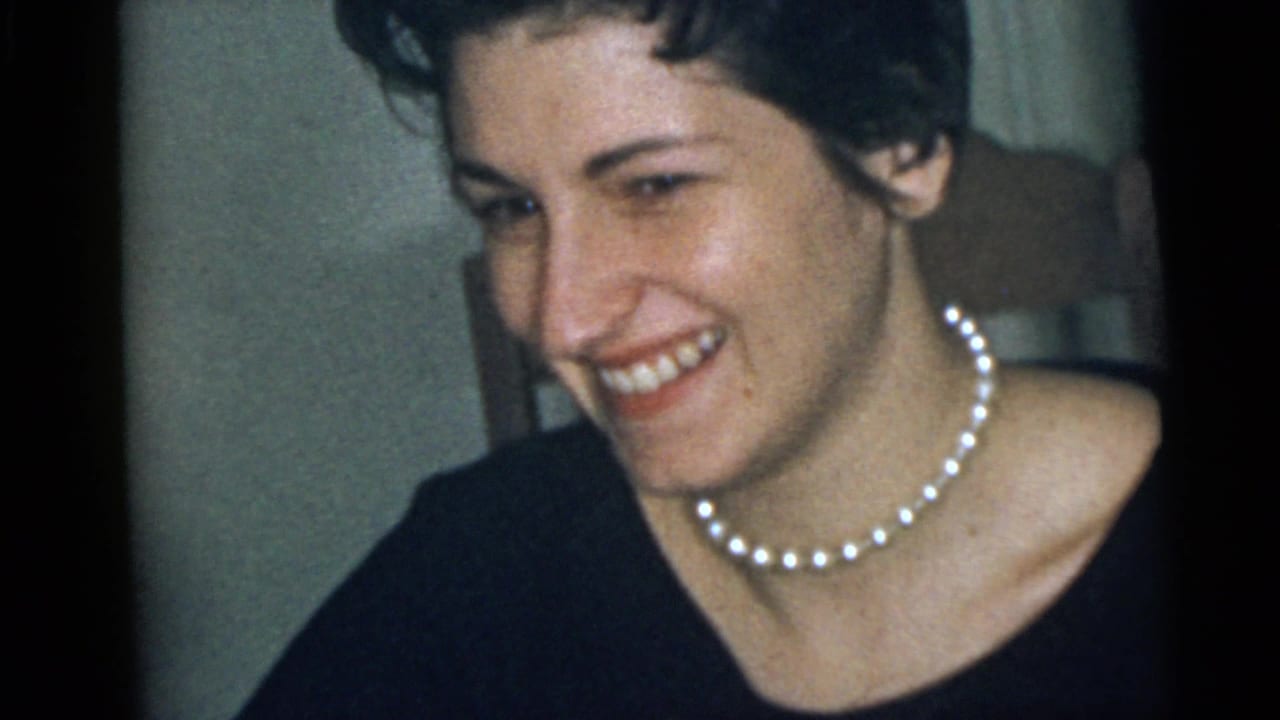 Adult woman laughing in a dark top with a pearl necklace visible.