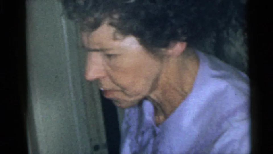 Older adult in a light purple top appears in profile indoors, following the close-ups in the 1960 Camden home-movie clip.