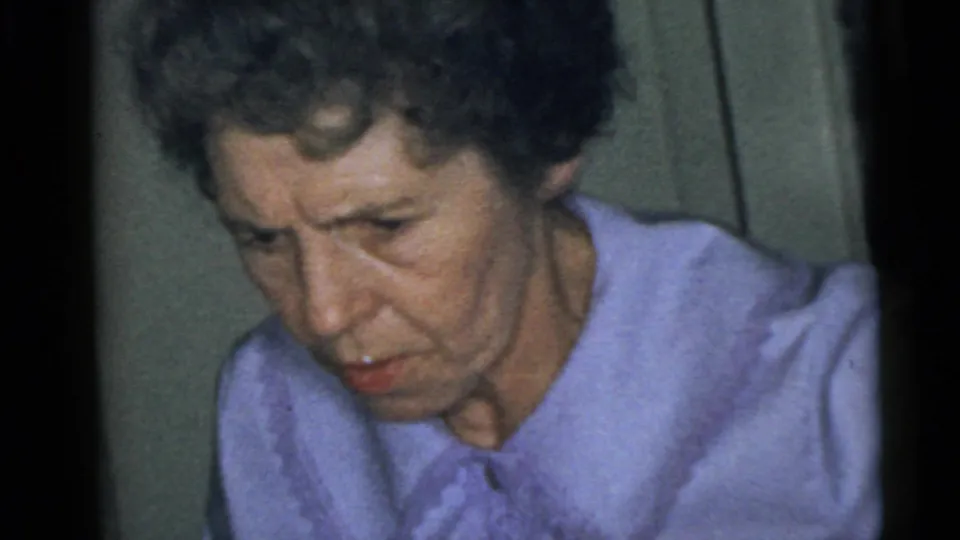 1960 Camden home-movie frame with a close view of an adult woman in a light purple collared shirt against a muted indoor wall.