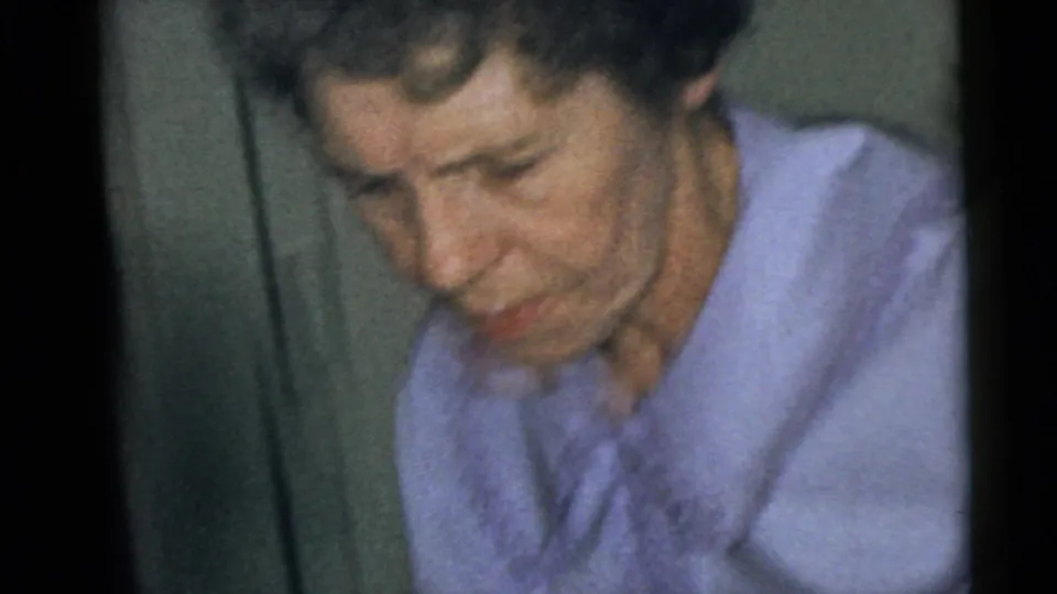 1960 Camden 8mm frame showing an adult woman in a purple collared blouse, softly focused and looking down inside a private room.