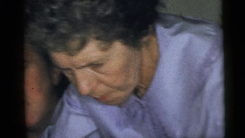 1960 Camden home-movie frame showing the woman in a light purple shirt looking down, with another person partly visible at the edge.